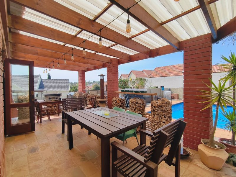 A covered outdoor patio featuring a timber pergola with translucent roofing, brick pillars, and tiled flooring, overlooking a private swimming pool.