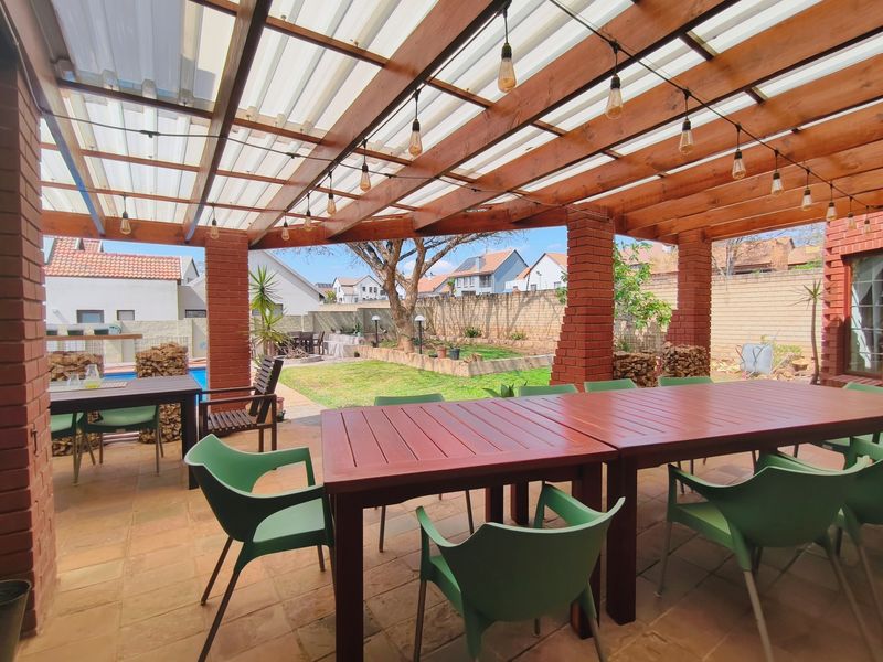 A spacious covered patio featuring a timber pergola with translucent roofing, brick support pillars, and tiled flooring, overlooking a private garden.