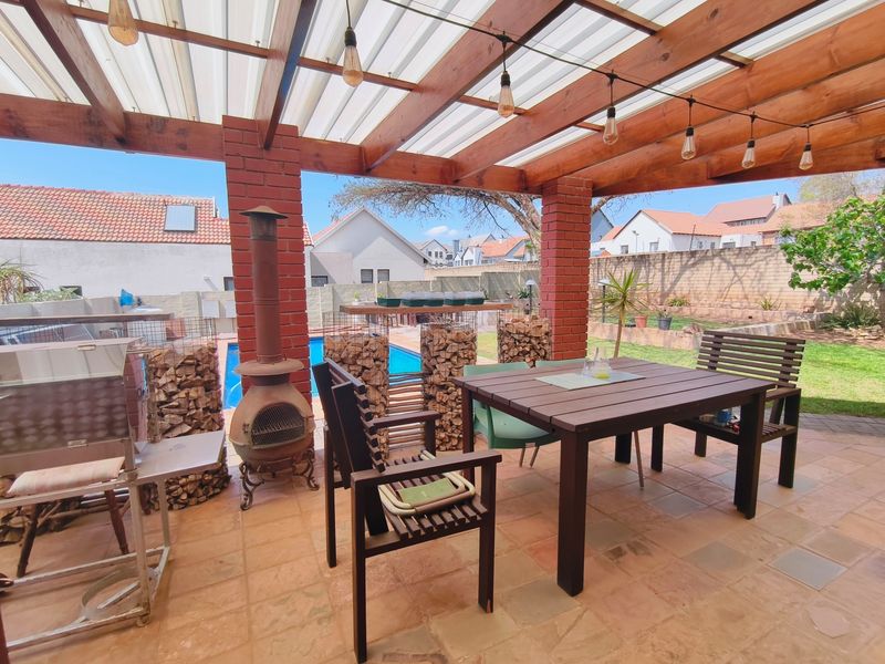 Covered outdoor patio area featuring a timber pergola, brick pillars, and direct access to a swimming pool and garden space.