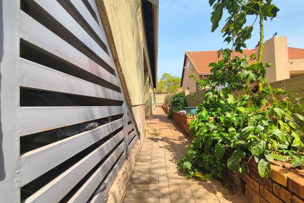 A side walkway featuring paved flooring, a brick retaining wall, and a slatted metal gate along the side of the property.