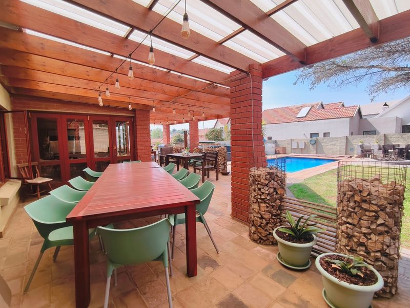 Spacious covered outdoor patio featuring a timber pergola with integrated lighting, brick and gabion pillars, overlooking a private swimming pool and garden area.