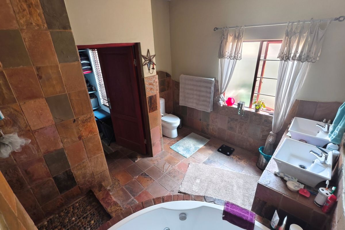 A spacious bathroom featuring a corner bathtub, walk-in shower, dual vanity basins, and natural stone-style wall and floor tiling.