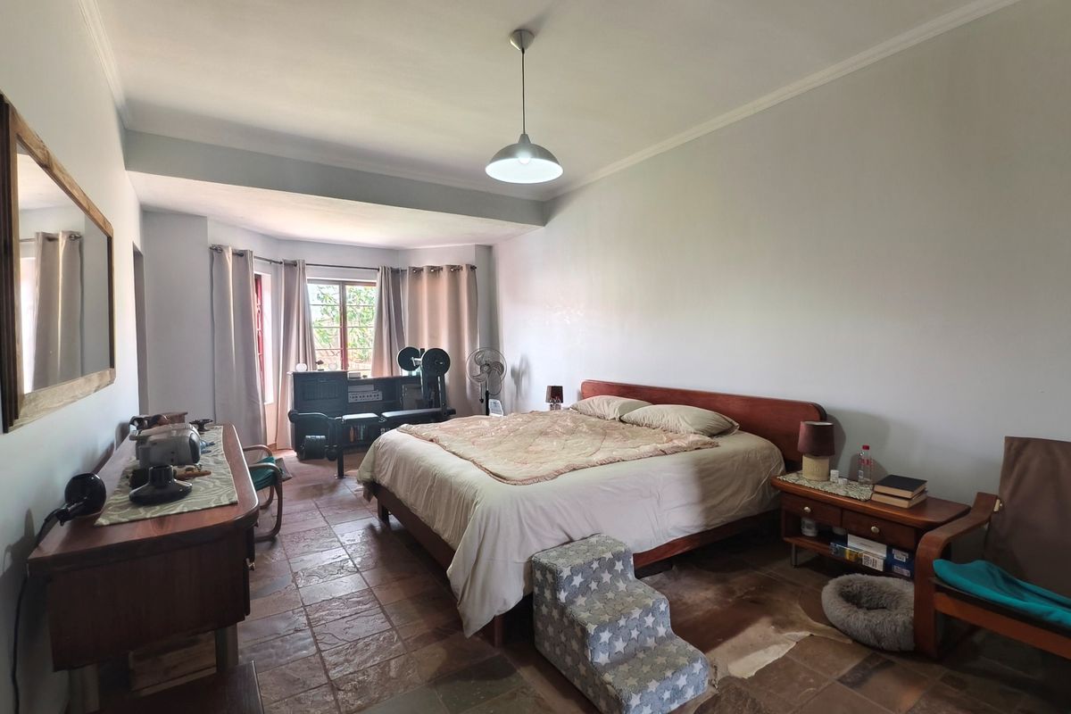 Spacious bedroom featuring terracotta tile flooring, a central pendant light, and a bay window that allows for natural light.