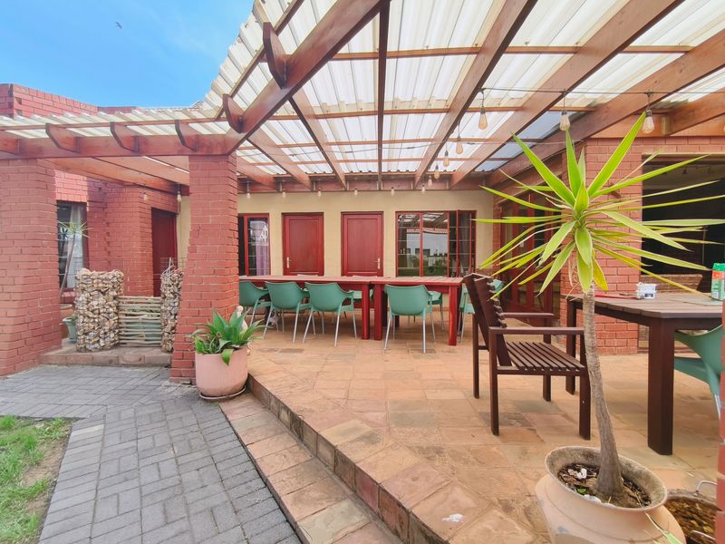 A covered outdoor patio area featuring a timber pergola with translucent roofing, brick pillars, and paved flooring, ideal for alfresco dining and entertaining.