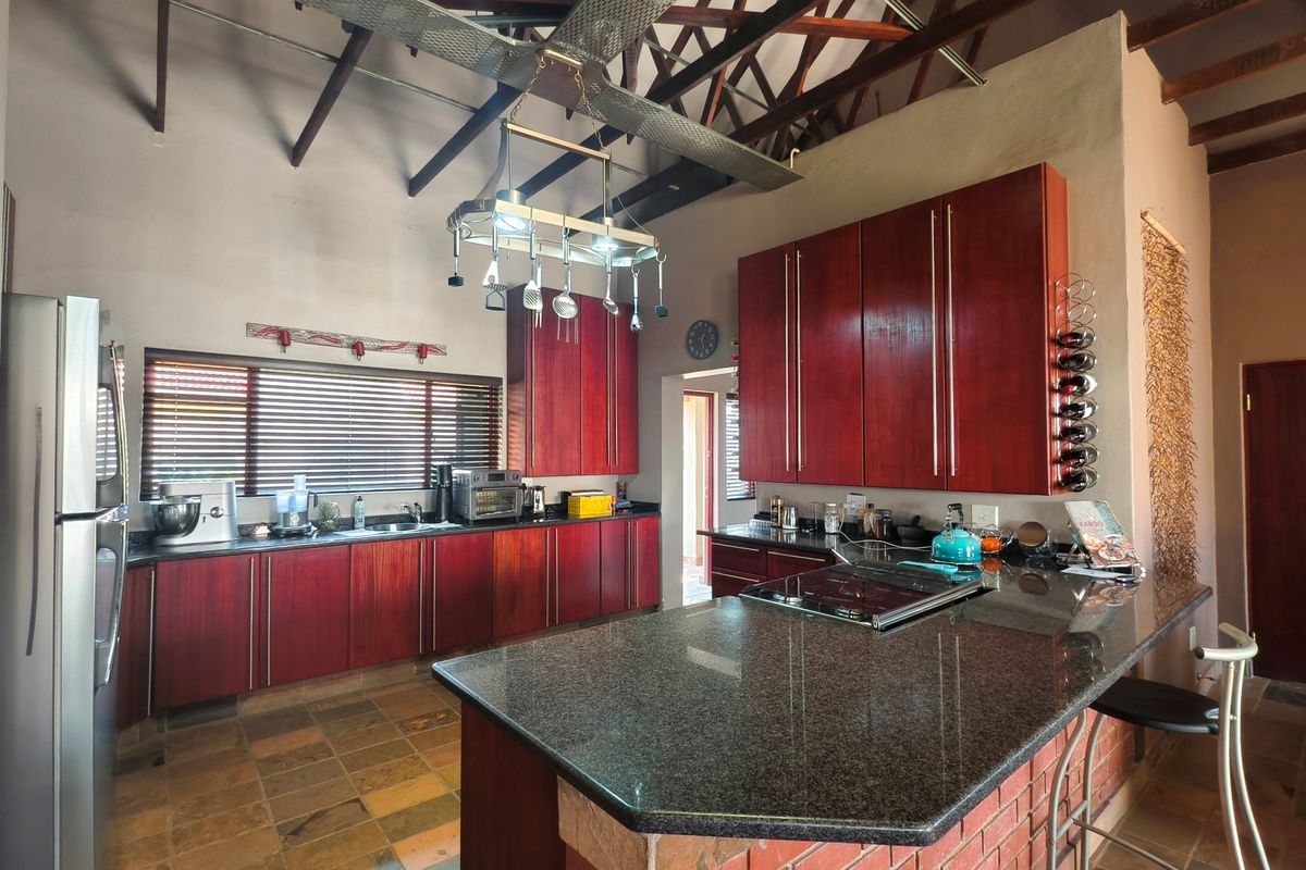 Spacious kitchen featuring rich red wood cabinetry, granite countertops, a brick-based island, and striking exposed timber roof trusses with slate flooring.