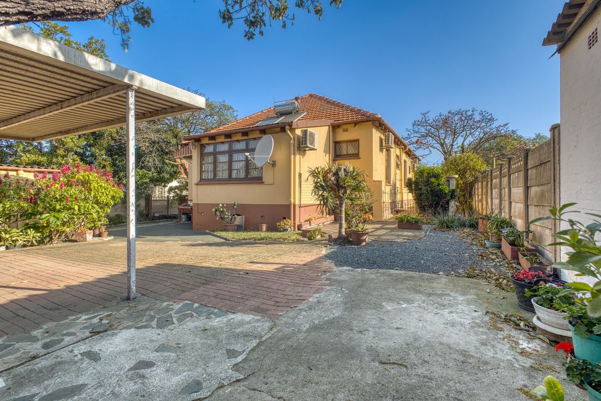 Rear exterior view of the house featuring a paved driveway, carport, solar water heater, and established garden area with perimeter walling.
