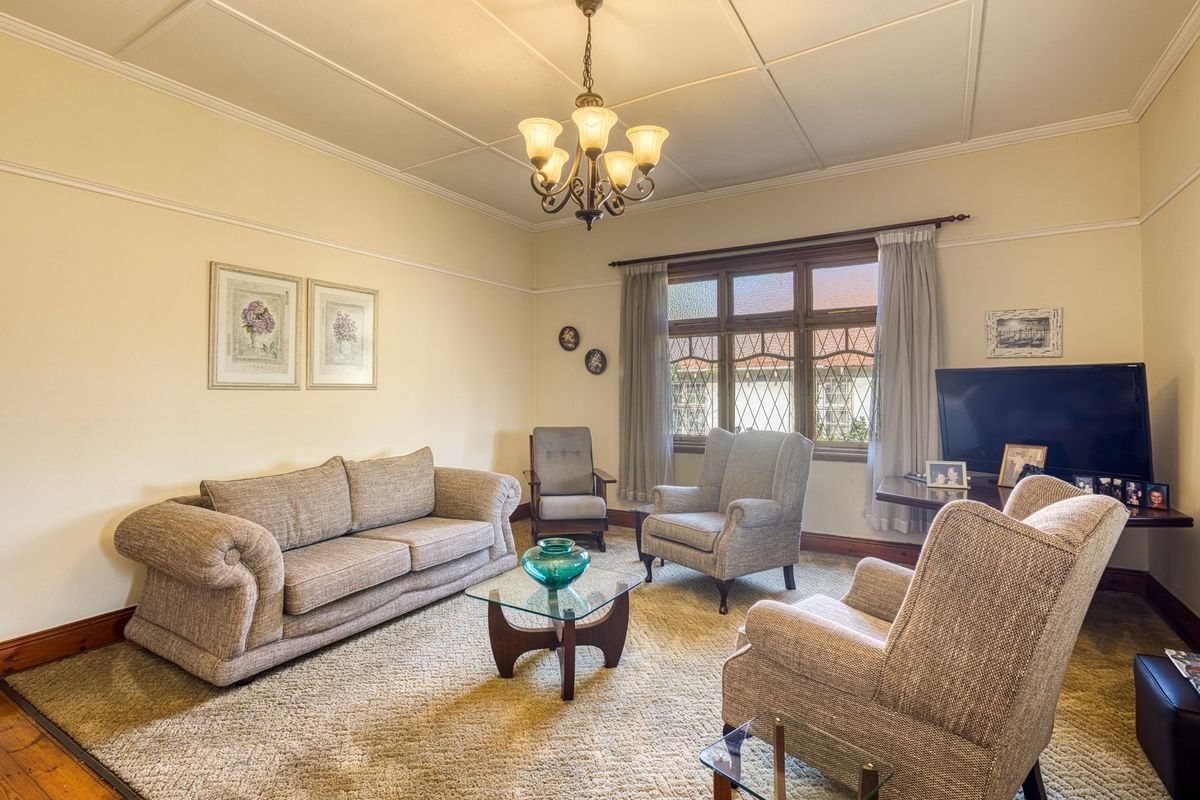 A traditional living room featuring classic leaded glass windows, timber skirting boards, and a decorative ceiling rose with a central chandelier.