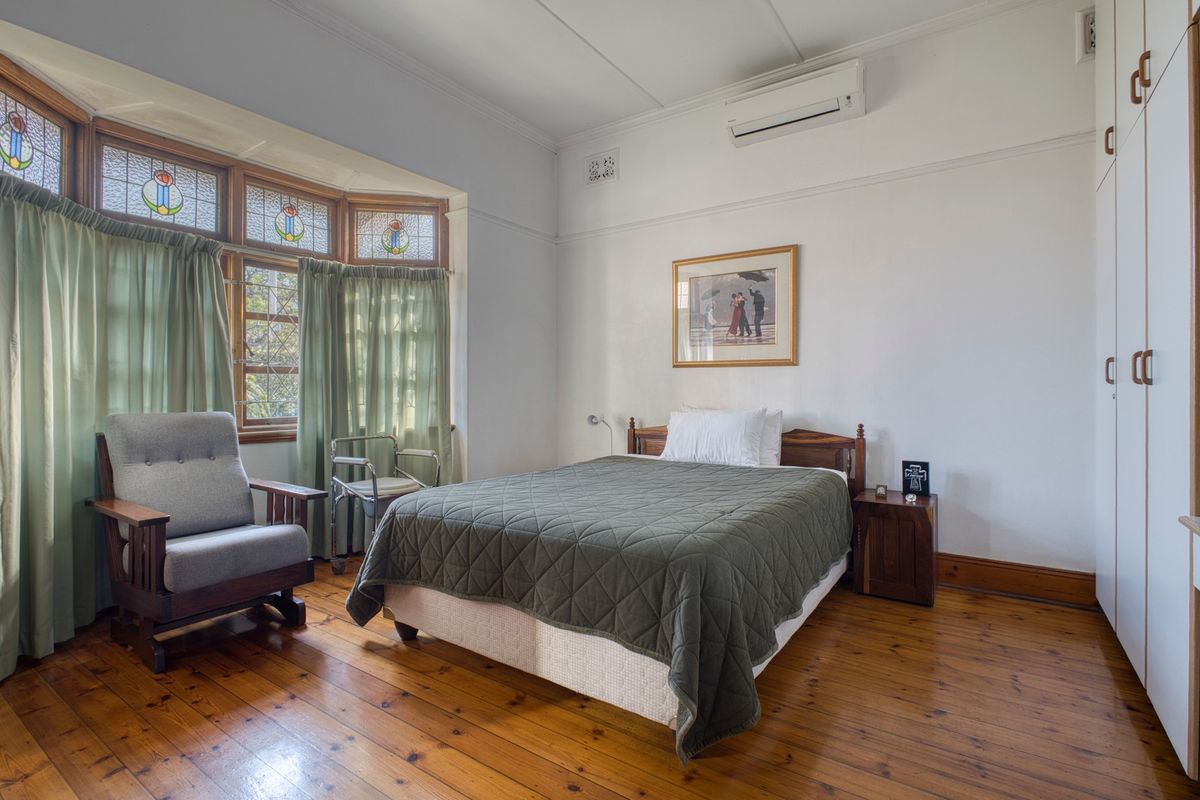 A well-maintained bedroom featuring polished timber flooring, a classic stained glass bay window, built-in wardrobe storage, and a wall-mounted split-system air conditioner.