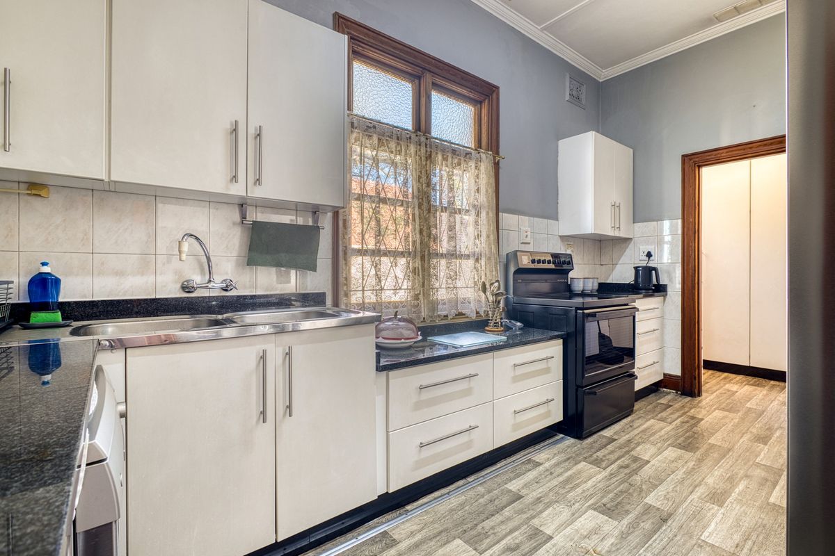 A functional kitchen featuring white cabinetry, granite countertops, a stainless steel sink, and a freestanding stove, complemented by wood-look laminate flooring.