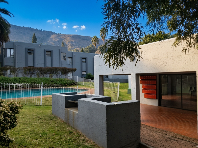 Communal pool area featuring a built-in braai, paved patio, and a bank of post boxes set against a backdrop of mountain views.