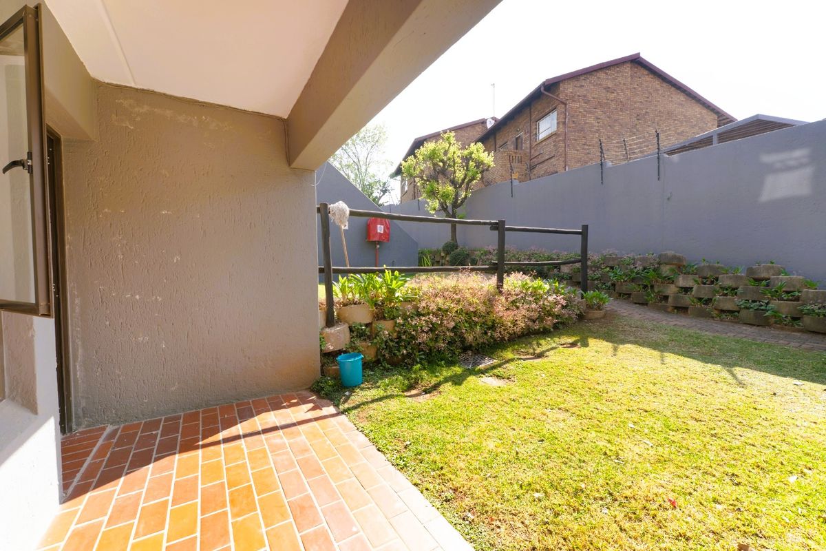 A private rear garden featuring a brick-paved patio, a small lawn area, and a tiered retaining wall with perimeter fencing.