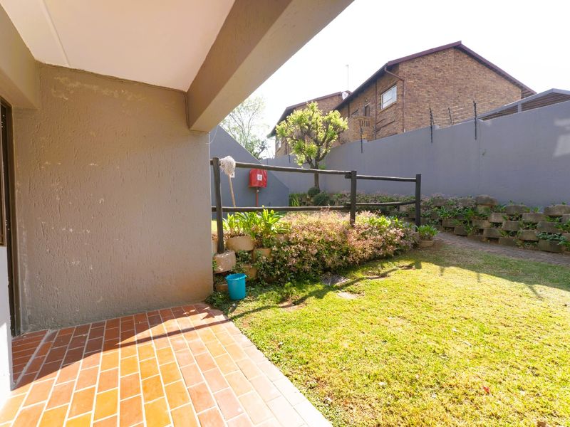 A private rear garden featuring a brick-paved patio, a small lawn area, and a tiered retaining wall with perimeter fencing.