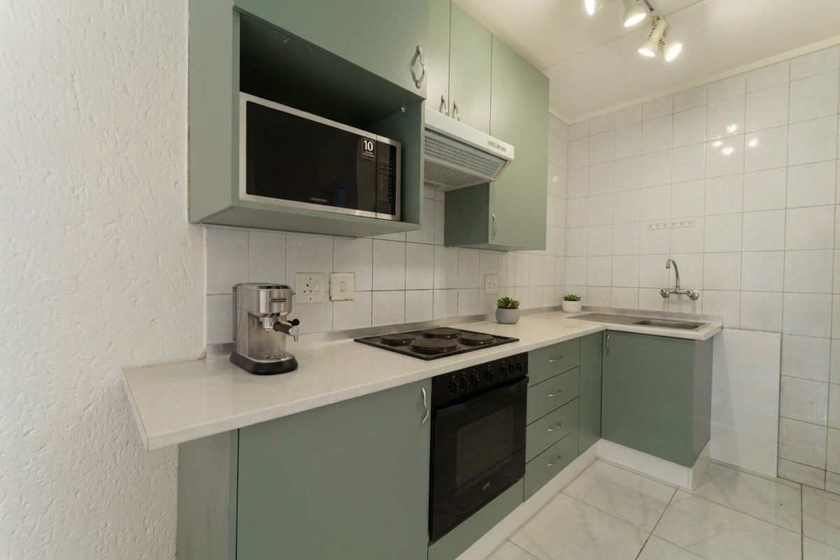 A functional kitchen featuring sage green cabinetry, a built-in oven with electric hob, extractor fan, and tiled finishes throughout.