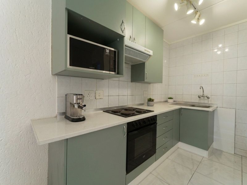A functional kitchen featuring sage green cabinetry, a built-in oven with electric hob, extractor fan, and tiled finishes throughout.