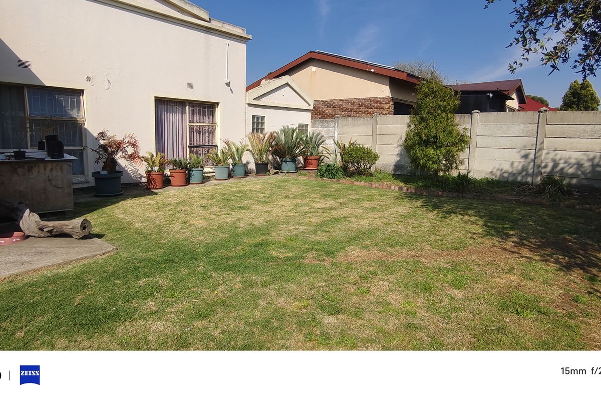 A rear garden view featuring a lawn, paved patio area, and concrete boundary wall.