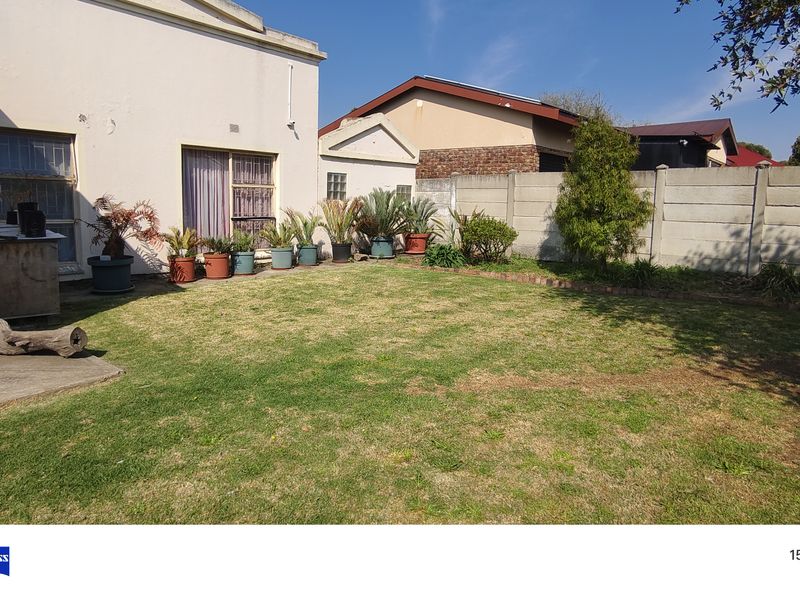 A rear garden view featuring a lawn, paved patio area, and concrete boundary wall.