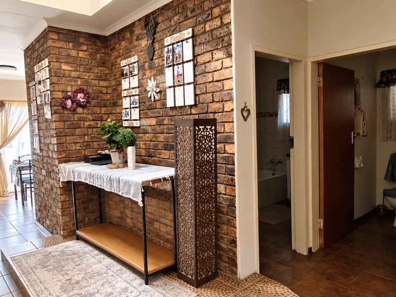 A hallway featuring an exposed brick wall, tiled flooring, and access to adjacent rooms through internal doorways.