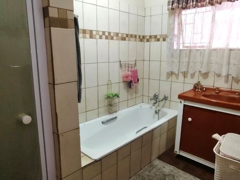 A functional bathroom featuring a built-in bathtub, a vanity cabinet with an integrated sink, and a separate shower enclosure with tiled walls.