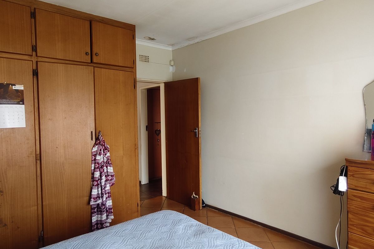 A bedroom featuring built-in wooden cupboards and tiled flooring, showing signs of wear and ceiling water damage.