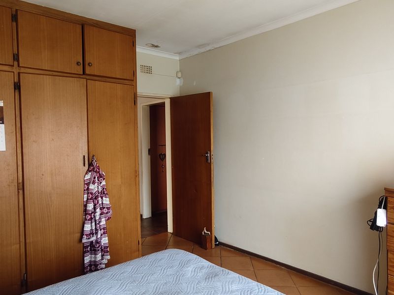 A bedroom featuring built-in wooden cupboards and tiled flooring, showing signs of wear and ceiling water damage.