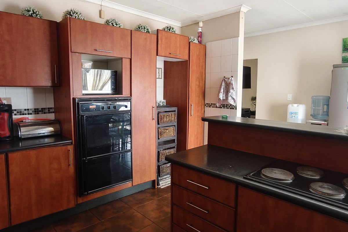 A functional kitchen featuring wood-finish cabinetry, built-in double oven, electric hob, and dark countertops with a tiled backsplash.