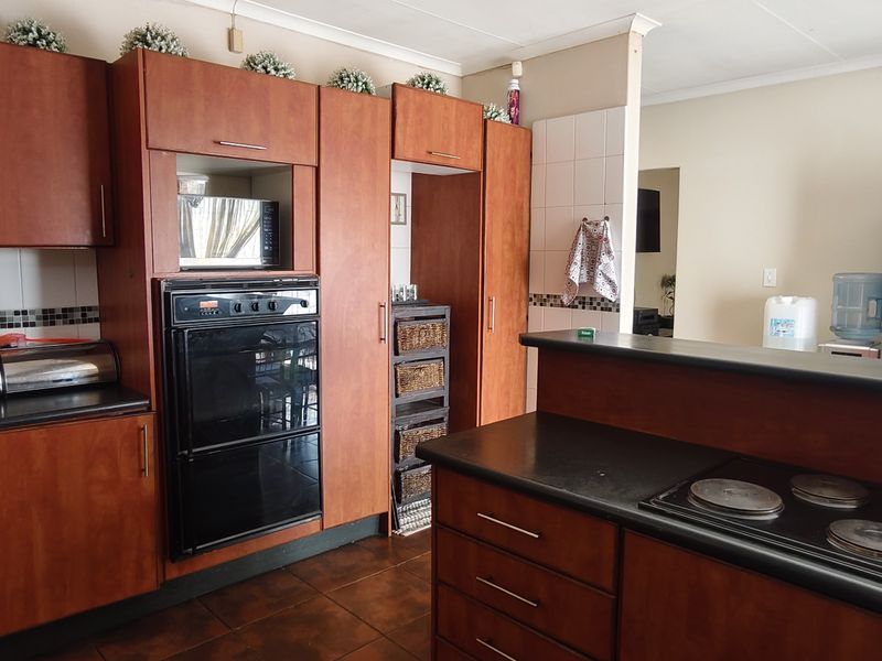 A functional kitchen featuring wood-finish cabinetry, built-in double oven, electric hob, and dark countertops with a tiled backsplash.