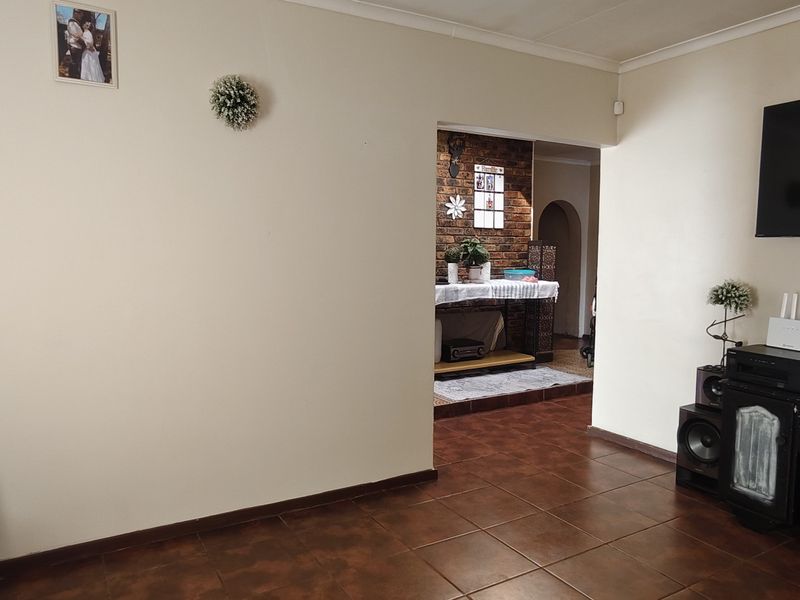 A living room featuring tiled flooring and an open transition to an adjacent space with an exposed brick wall feature.