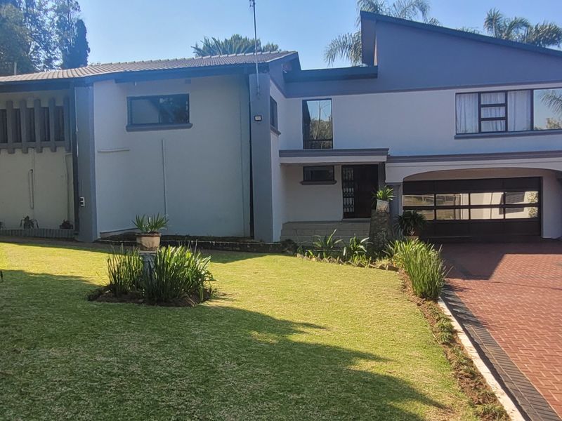 Front elevation of a modern double-story house featuring a paved driveway, double garage, and an upper-level balcony overlooking a well-maintained front lawn.