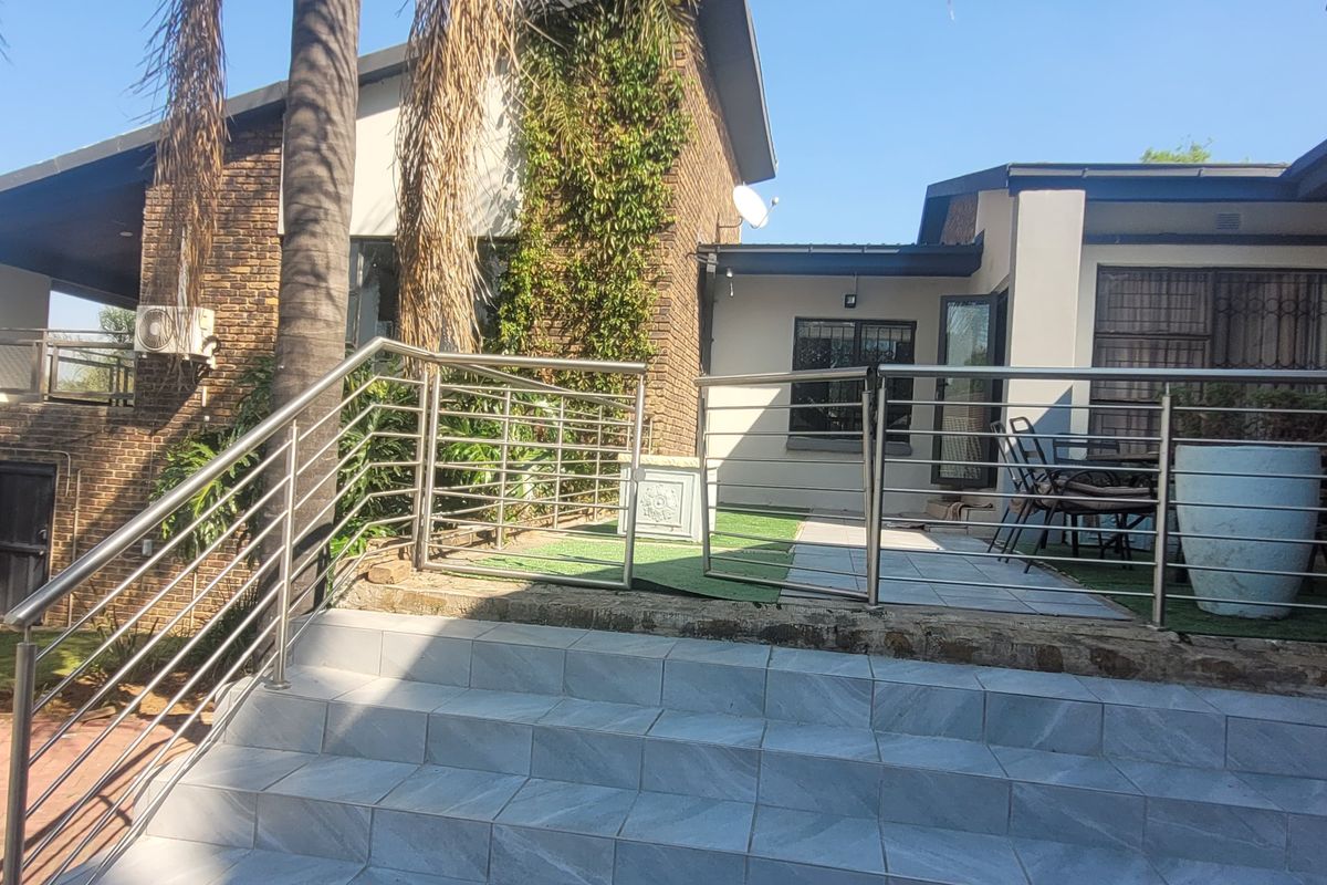 Rear exterior view featuring a tiled staircase with stainless steel balustrades leading to a paved patio area and garden space.