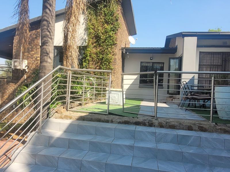 Rear exterior view featuring a tiled staircase with stainless steel balustrades leading to a paved patio area and garden space.