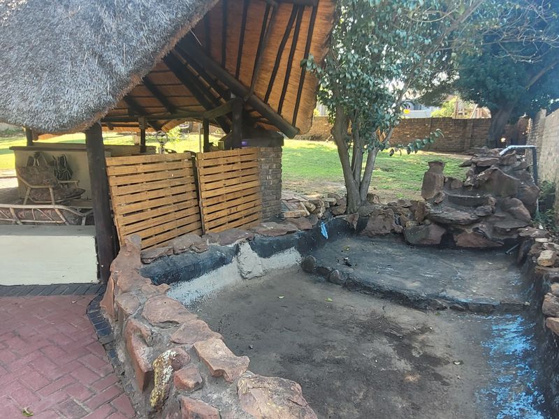 Outdoor entertainment area featuring a thatch lapa, built-in bar, and a stone-clad water feature with an empty pool basin requiring maintenance.