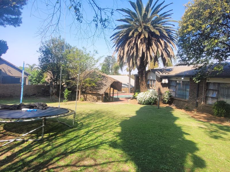 Spacious rear garden featuring a brick-built house, a thatched lapa, and a swimming pool, set within a well-established residential yard.