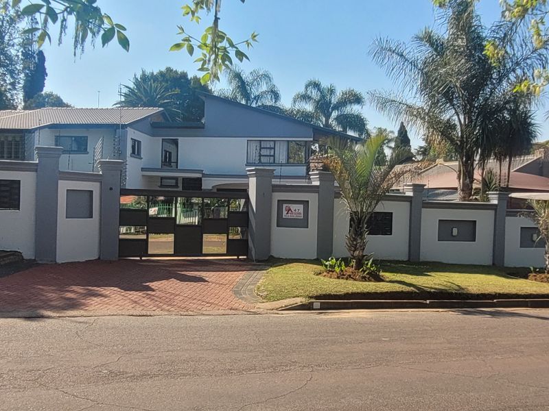 Front view of the property featuring a secure perimeter wall, gated entrance, paved driveway, and well-maintained garden area.