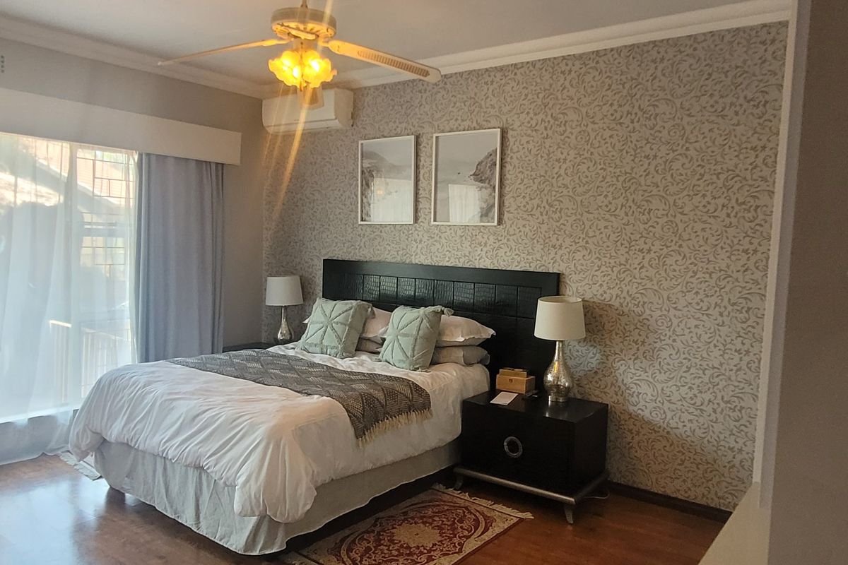 A well-maintained bedroom featuring laminate flooring, a ceiling fan, and a wall-mounted air conditioning unit.