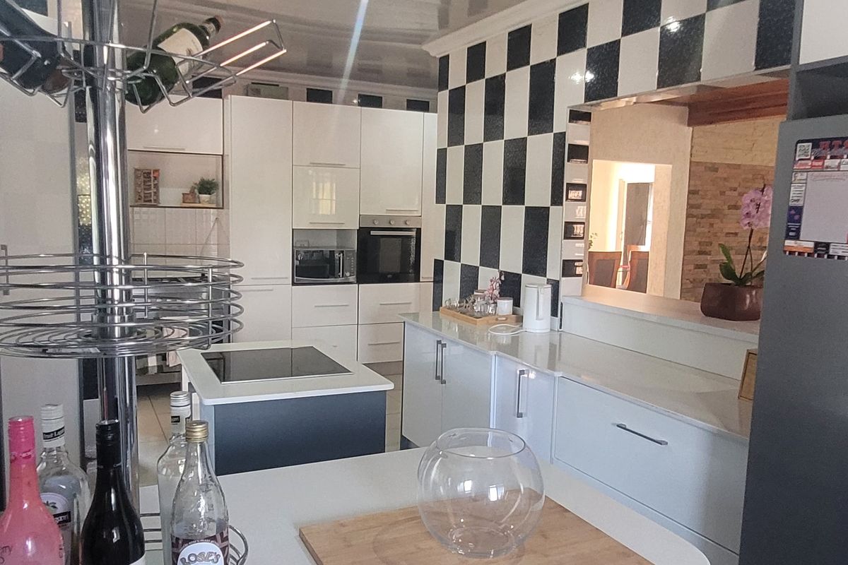 Modern kitchen featuring white cabinetry, quartz countertops, a central island, and a distinctive black and white checkered tiled backsplash.