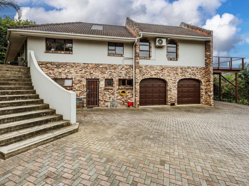 Front exterior view of a two-story house featuring a brick facade, double garage, paved driveway, and a concrete staircase leading to the upper level.