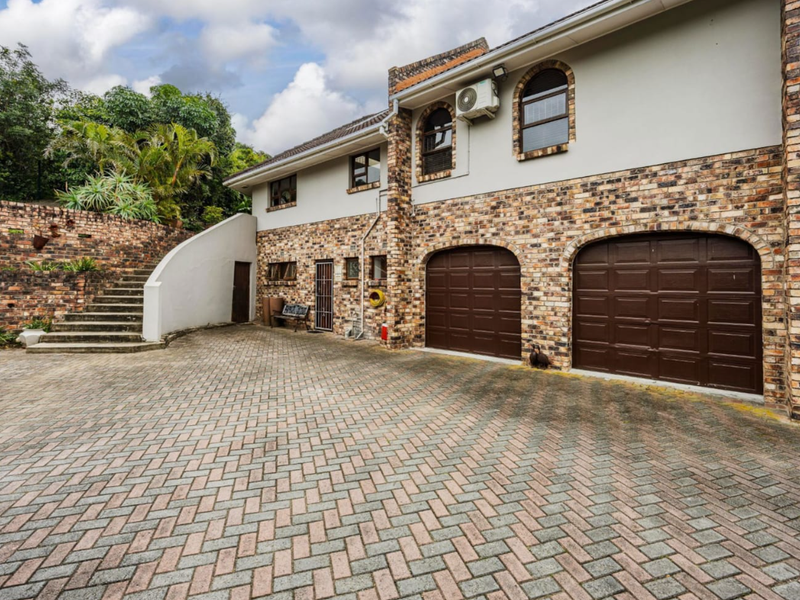 Front exterior view featuring a double garage, paved driveway, brick facade, and a concrete staircase leading to the upper level.
