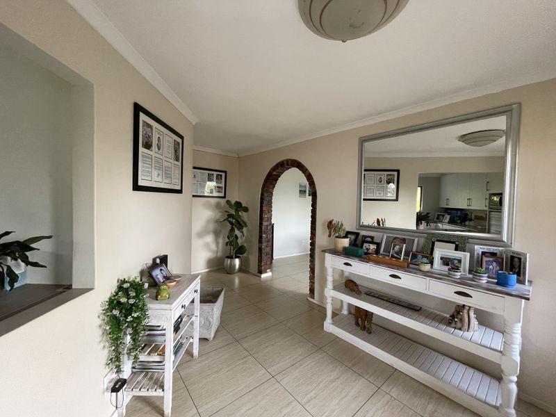 A bright hallway featuring neutral tiled flooring, a distinctive brick archway leading to adjacent rooms, and coved ceiling detailing.
