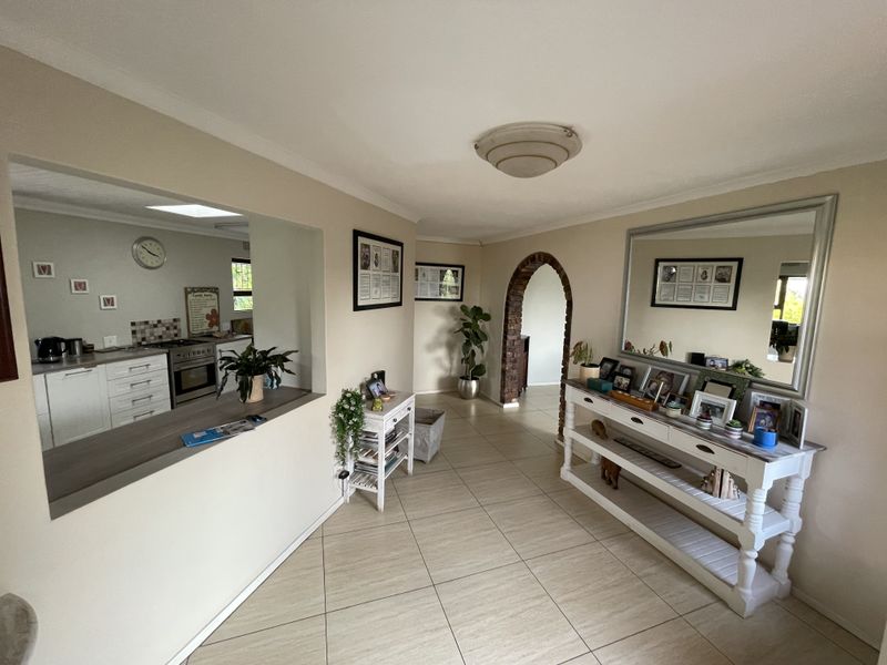 Open plan living area featuring tiled flooring, a distinctive brick archway, and a convenient pass-through window connecting to the kitchen.