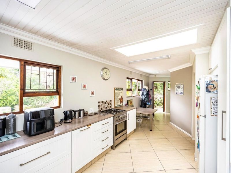 A functional kitchen featuring white cabinetry, gas stove, tiled flooring, and a skylight, providing a bright and practical workspace.