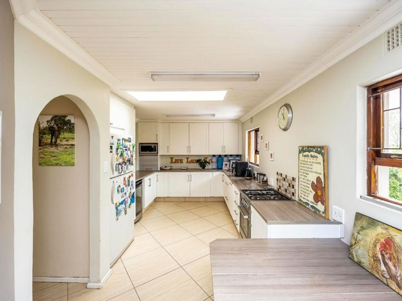 Functional kitchen featuring white built-in cabinetry, gas hob, built-in oven, laminate countertops, and a skylight, with tiled flooring throughout.