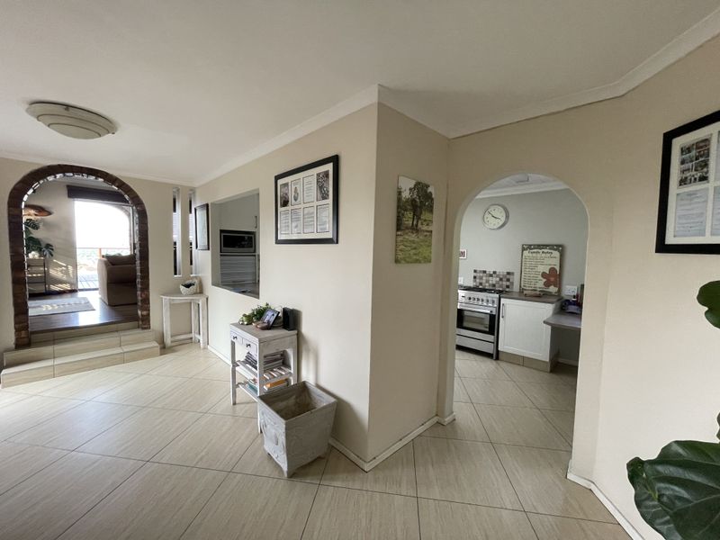 Open plan living area featuring tiled floors, a distinctive brick archway leading to a patio, and a functional kitchen with built-in cabinetry and oven.