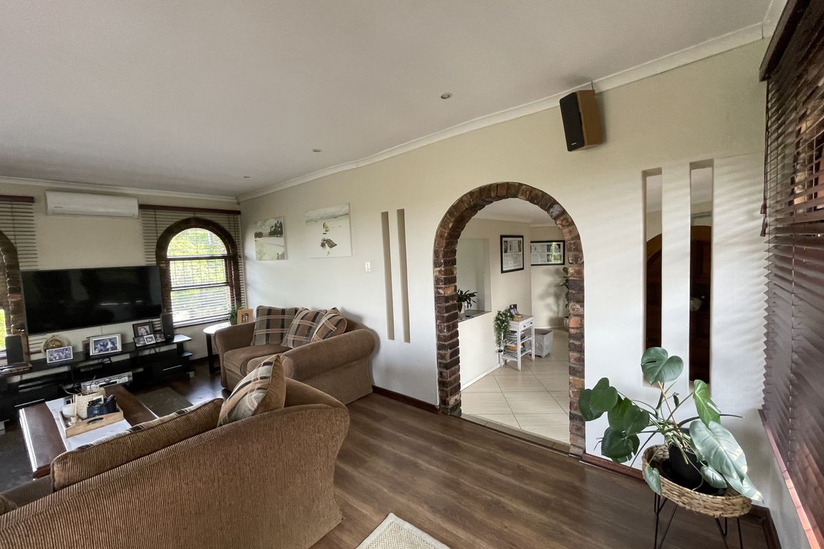 A comfortable living room featuring laminate flooring, a distinctive brick archway, arched windows with venetian blinds, and a wall-mounted split-system air conditioner.