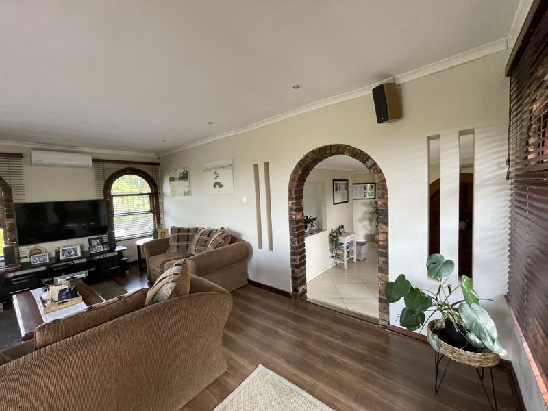 A comfortable living room featuring laminate flooring, a distinctive brick archway, arched windows with venetian blinds, and a wall-mounted split-system air conditioner.