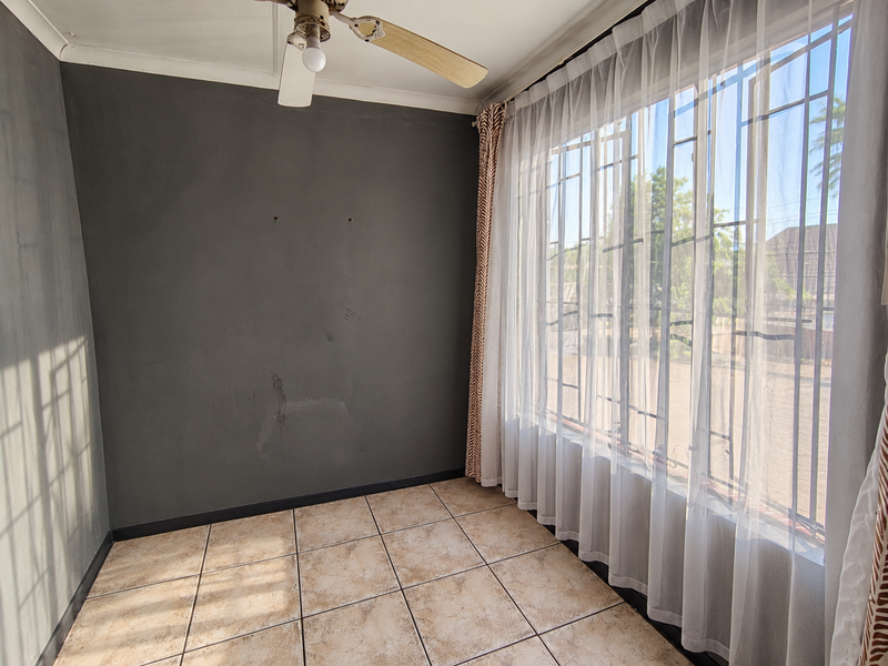 An empty bedroom featuring tiled flooring, a ceiling fan, and large windows fitted with security bars and curtains.