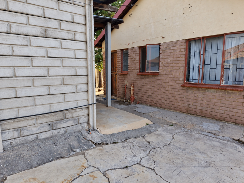 Rear exterior view of the property featuring brick walls, security bars on windows, and a concrete paved area showing signs of wear and cracking.