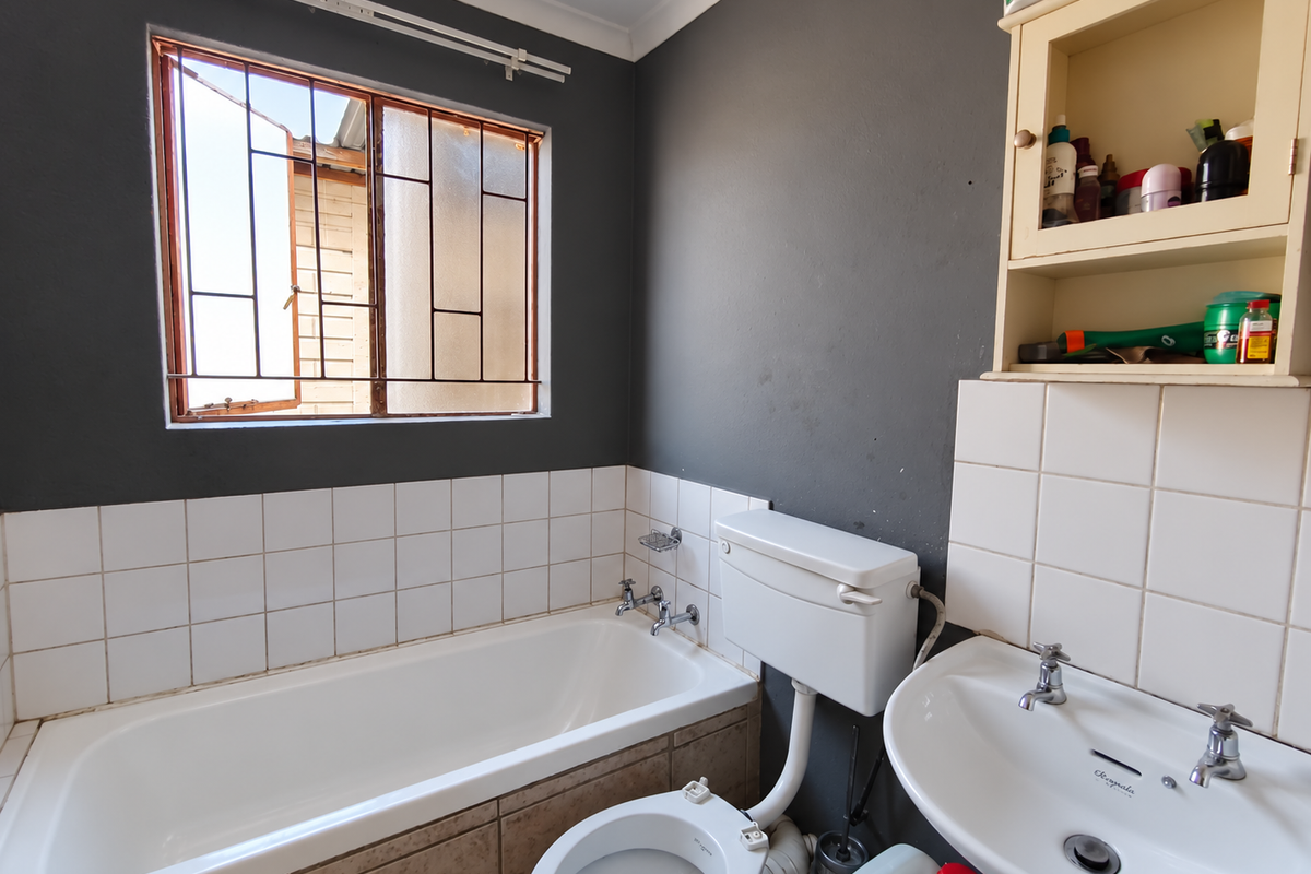 A functional bathroom featuring a built-in bathtub, pedestal washbasin, and toilet, with dark grey walls and tiled splashbacks. Requires cosmetic updates.
