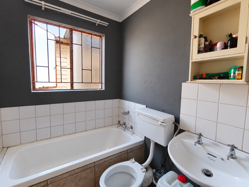 A functional bathroom featuring a built-in bathtub, pedestal washbasin, and toilet, with dark grey walls and tiled splashbacks. Requires cosmetic updates.