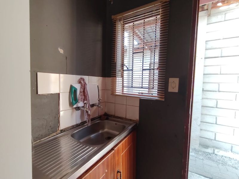 A compact scullery area featuring a stainless steel sink, wooden cabinetry, and tiled splashback, requiring some cosmetic repairs to the wall finishes.