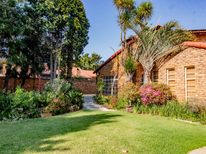 A well-maintained rear garden featuring a face brick house facade, established landscaping, and a paved pathway leading through the lush green lawn.